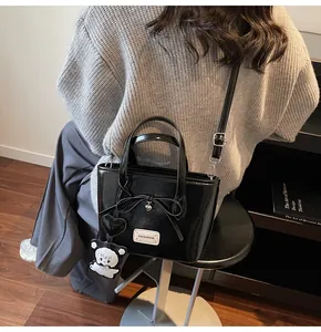 Detail of black glossy bucket bag with heart pendant and cute bear charm on shoulder strap
