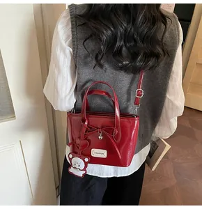 Close-up of red patent leather bucket bag with bow and bear charm worn by a model