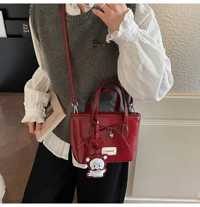 Detail of red glossy bucket bag featuring fashion patch, bow, and bear pendant charm