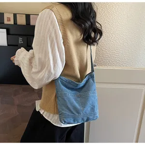 Détail d'un sac cabas en jean bleu délavé avec poche avant porté à l'épaule