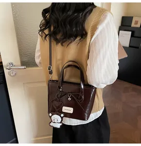 Detail of dark brown glossy bucket bag featuring a cute bear charm and heart pendant