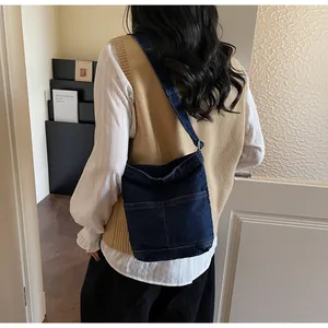 Détail d'un sac seau en denim bleu foncé avec deux poches avant et de larges brides