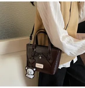 Detail of dark brown glossy patent leather bucket bag with cute bear charm and bow