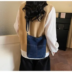 Détail du sac bandoulière en denim bleu foncé avec deux poches sur une tenue décontractée