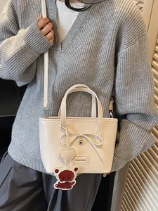 Minimalist beige bucket bag with brown bear charm and bow detail shown on a model