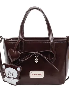 Minimalist dark brown bucket bag with bow detail and silver heart pendant on white background