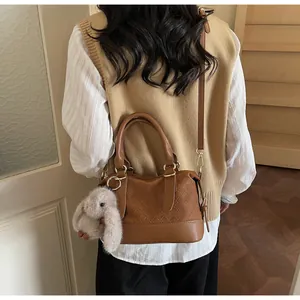 Detail of brown woven faux leather handbag featuring a plush bunny charm and golden hardware