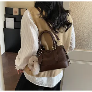 Detail of a brown leather bag with quilted texture, gold hardware, and a plush bunny charm