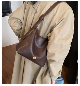 Détail du sac cabas en cuir marron foncé avec logo doré porté par un mannequin