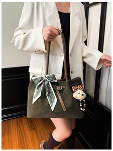 Close-up of dark green suede tote bag with silk scarf and cute plush bear charm