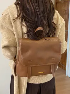 Zaino vintage in pelle marrone con dettagli dorati indossato da una modella all'aperto