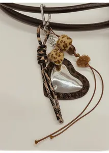 Détail d'un bijou de sac cœur léopard avec pompons sur une bandoulière marron