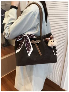 Detail of dark brown tote bag with decorative silk scarf and plush bear charm on model