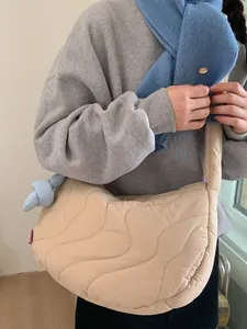 Borsa tote trapuntata beige a forma di mezzaluna con tracolla imbottita indossata da una persona