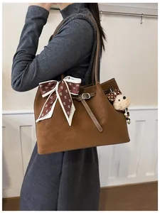 Detail of a brown suede tote bag with fashion scarf and plush bear charm on model