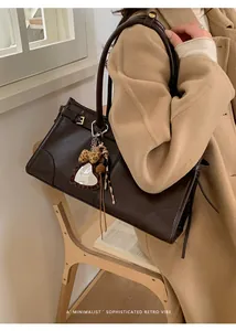 Détail d'un sac cabas en cuir marron foncé avec un charm coeur en peluche porté à l'épaule