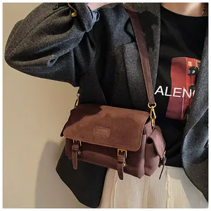Detailed view of dark brown suede messenger bag with gold buckles and retro strap