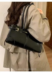 Gros plan d'un sac cabas noir brillant avec boucle dorée sur un mannequin en trench-coat