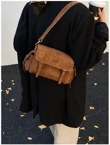 Detail of brown suede crossbody bag with gold buckles worn over a black winter coat