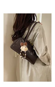 Side view of dark brown leather shoulder bag with plush puppy charm on female model