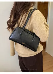 Detail view of black textured leather Boston bag with golden minimalist fashion lettering