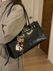 Sac cabas chic en similicuir noir avec boucle métallique et charms porté à l'épaule