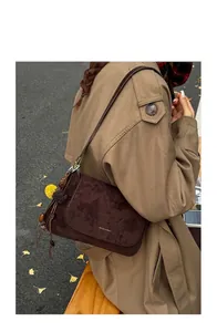 Detail der dunkelbraunen Wildleder-Baguette-Tasche mit Blumenanhänger an einem Modell