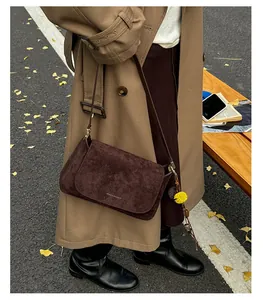 Detail einer dunkelbraunen Wildleder-Baguette-Tasche mit Riemen und Blumen-Anhänger