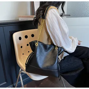 Detail of black quilted tote bag with golden chain strap and drawstring accents