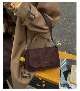 Detail einer dunkelbraunen Wildleder-Baguette-Tasche mit Goldschnalle und gelbem Anhänger
