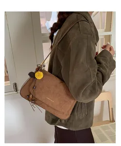 Detail einer dunkelbraunen Wildleder-Baguette-Tasche mit Blumenquaste und Goldlogo
