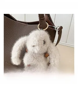 Close-up of plush rabbit charm with leather details on a brown pebbled leather handbag