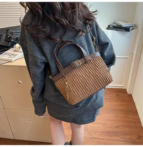 Detail of a brown pleated leather bucket bag with a golden key charm and top handle