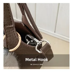 Detail of silver hardware hook and gray plush ball on brown pebbled leather bag