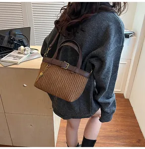 Detail of a brown pleated bucket bag with a leather handle and a gold key charm accent