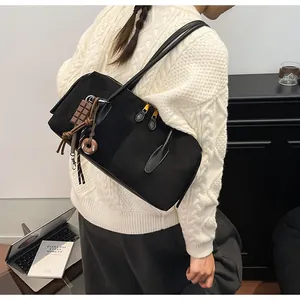 Détail du sac cabas en daim noir avec breloques fantaisie sur un pull en maille blanc