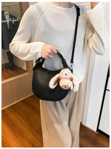 Detail view of black pebble leather moon bag with plush rabbit charm and STONEY logo