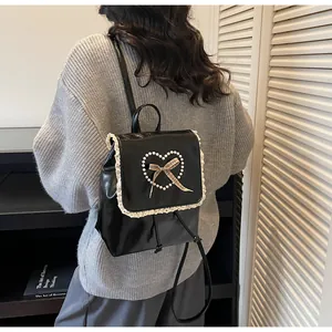 Detail of black faux leather backpack featuring lace trim and pearl heart motif
