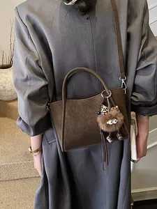 Brown vintage soft leather bucket bag with plush monster charm on a gray trench coat