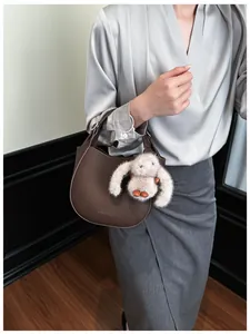 Detail of dark brown leather bucket bag with logo and cute plush bunny charm