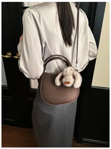 Brown litchi grain leather bucket bag with cute plush rabbit charm on a silk shirt model