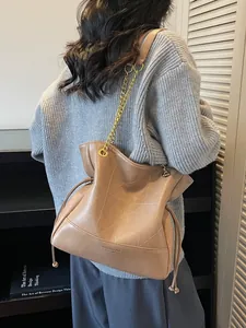 Brown bucket bag with white geometric stitching and gold chain strap in use