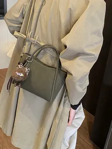 Minimalist dark green leather bucket bag with leopard bow plush pendant on khaki coat model