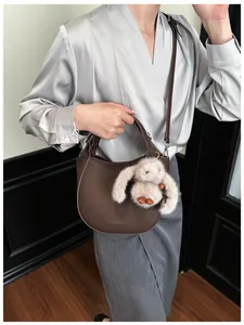 Brown lychee leather bucket bag with plush rabbit charm and adjustable shoulder strap