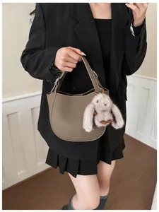 Close-up of taupe grain leather handbag with a plush rabbit charm on a stylish model