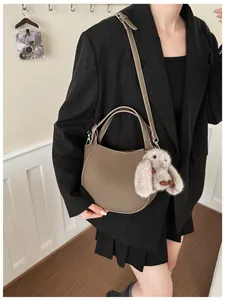 Detail of khaki leather crescent bag with plush rabbit charm and crossbody strap