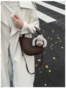 Detail of a dark brown hobo bucket bag with litchi texture and a grey plush rabbit charm