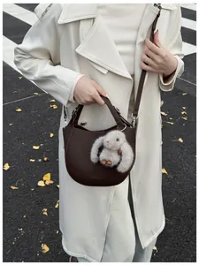 Detail of dark brown leather bucket bag with plush rabbit charm and crossbody strap