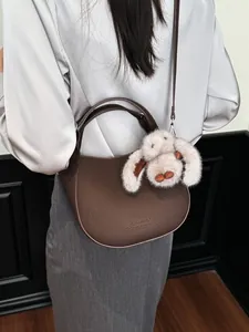 Dark brown pebbled leather crescent bucket bag with a plush rabbit charm accessory