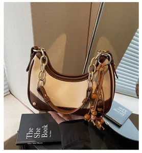 Detail of hobo bag with gold chain and wooden bead tassel against a soft warm light background